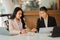 Two Asian female accountants working in the office with laptop computers and financial documents on the table.