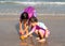 Two Asian girl use plastic toy dig sand at sea. Sibling in swimming suit. Favorite activity in summer