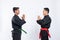 Two Asian men wearing pencak silat uniforms stand opposite each other with mutual respect