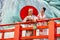 Two Asian pretty women stay close to red railing in the area of base of green big buddha statue also look at camera with smiling