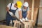 Two  Asian repairmen wearing safety helmet , working in wood workshop , cutting wooden plank with hand saw