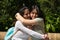 Two Asian women on holiday. They are sitting in a park and are hugging each other tightly. On their legs is a tourist map of the