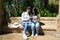 Two Asian women on holiday. They are sitting in a park looking at the pictures on the camera. On her legs she is holding a tourist