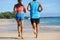 Two athletes runners couple running together on beach. People from behind jogging away barefoot on sand on tropical
