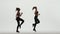 Two athletic cheerleaders in shiny tops and leggings are dancing in sync on a white studio background. Cheerleading