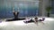 Two athletic women stretching legs, leans forward sitting on a splits on mat in the gym near half-transparent wall