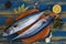 Two atlantic mackerel fishes ready for cooking on the wooden board decorated with spices and lemon slice on the blue wooden table