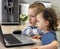 Two attentive and surprised children are sitting in the kitchen and looking at the computer