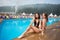 Two attractive brunette women wearing bikini posing near the swimming pool, making selfie photo with selfie stick