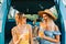 Two attractive cheerful women drinking lemonade near van, enjoying summer vibes in road trip