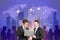 Two attractive european businessmen using laptop together on abstract blue city background with crowd and map. Teamwork, global