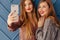 Two attractive stylish young girls with phone on simple aqua background