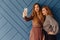 Two attractive stylish young girls with phone on simple aqua background