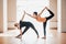 Two attractive young women balancing and practicing yoga in a light studio. Well being, wellness concept. One of the woman is plus