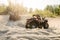 Two atv riders in helmets ride in a circle on sand