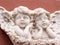 Two baby angels with wings marble sculpture on red wall of building. Close-up, front view
