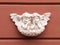 Two baby angels with wings marble sculpture on red wall of building. Close-up, front view