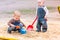 Two baby boys playing with sand in a sandbox