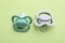 Two baby pacifiers on pale green background