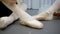 Two ballerinas are tying tape of pointe shoes sitting on floor in school.