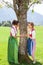 Two bavarian women cling to a tree and smile at each other