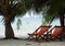 Two beach chairs on beach under palm-trees near the sea