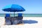 Two beach chairs under a blue umbrella on a white sandy beach