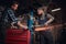 Two bearded auto mechanic in a uniform and safety glasses working with an angle grinder while standing under lifting car