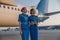 Two beautiful air hostesses in blue uniform smiling away, standing in front of a big passenger airplane in airport at