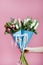 Two beautiful bouquet of tulips and roses in blue packing in a female hand on pink background