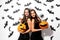 Two beautiful brunette women in black dresses have fun with jack-o-lanterns on a white background with bats and spiders