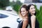 Two beautiful businesswomen in black outfut smiling and posing. Portrait of girls in front of electric car charging in the