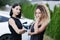 Two beautiful businesswomen in black outfut smiling and posing. Portrait of girls in front of electric car charging in the