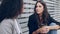 Two beautiful businesswomen talking while drinking coffee sitting on a bench on the street.