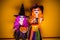 Two Beautiful girl in a witch costume on a yellow background scaring and making faces