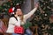 Two beautiful girls in hats Santa hats are shooting a selfie near the Christmas tree.