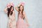 Two beautiful girls stand in a studio, play silly and have circlets of flowers on their heads. They wear light silk