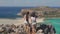 Two beautiful girls standing on edge of cliff. Female friends admire view of blue sea lagoon and rocky beach, pointing