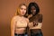 Two beautiful international female, wearing same beige bra, having surprised shocked looks, african girl pointing finger