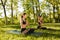 Two beautiful ladies in black sporty tops and leggings sitting in lotus poses and meditating together