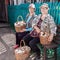 Two beautiful mature women sit on a bench near the house with baskets of mushrooms