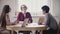 Two beautiful positive Caucasian girls talk to Japanese man at a job interview by the table in modern healthy office.