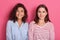 Two beautiful smiling girls with dark hair posing against pink background, looking directly at camera, wearing casually, ladies