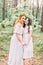 Two beautiful stylish happy bridesmaids in white dresses and wreaths on heads, smiling, holding hands and embracing