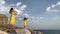 Two beautiful twin sisters violinists in yellow concert dresses are playing electric violins on rocks by the Mediterranean sea in