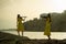 Two beautiful twin sisters violinists in yellow concert dresses are playing electric violins on sunset on rocks by the