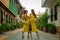 Two beautiful twin sisters violinists in yellow concert dresses are posing with electric violins on narrow Ottoman street of old