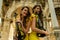 Two beautiful twin sisters violinists in yellow concert dresses are posing with electric violins near Hadrian`s gate in old town