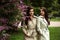 Two beautiful twins young women in trench coats near blooming lilac