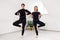 Two beautiful women are doing Pilates in a bright studio. Slender flexible athletes in black suits do exercises with